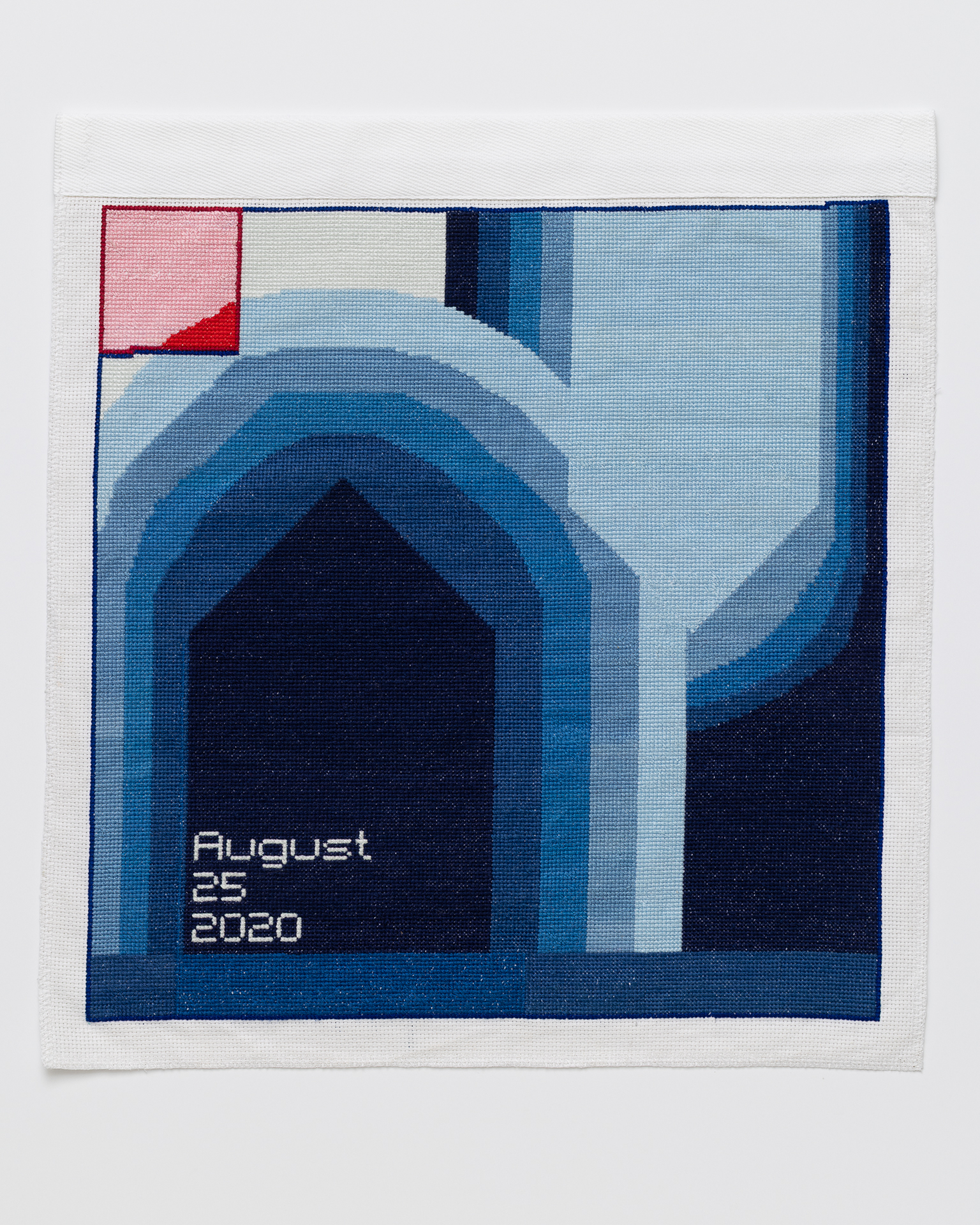 Cross stitch embroidery of abstsract blue shapes in varying colors. Dark arch shape on the left side outlined with lighter shades of blue. "August 25 2020" written in bottom left. Light pink square in top left.
