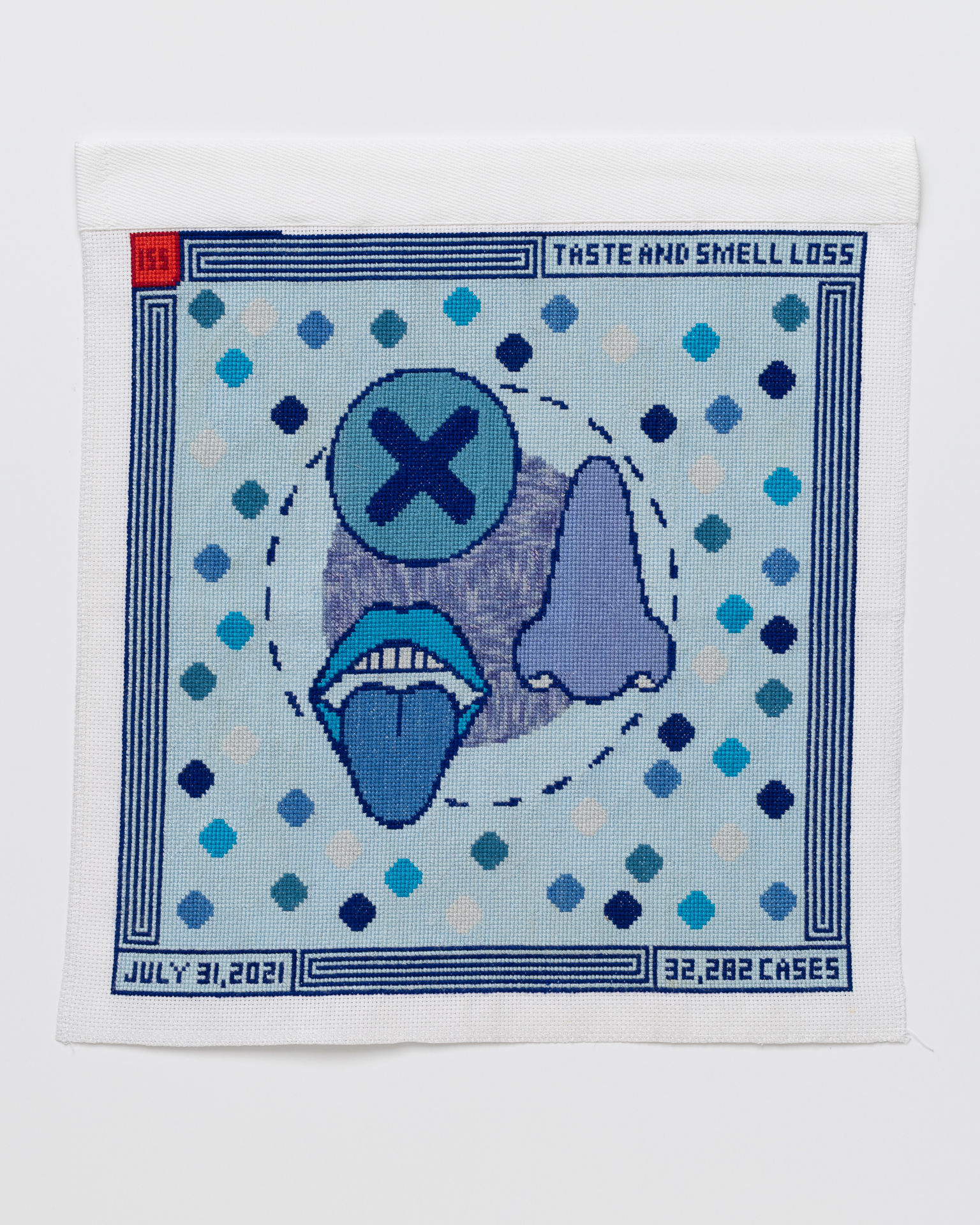 Cross stitch embroidery with a few circles in the middle. One circle has a dark blue "X" in it. A mouth with the tongue sticking out and a nose are stitched on top. The back ground is light blue with multicolored dots sprinkled around, with a darker blue striped border. There is a red square in the top left corner with "155" inside, "TASTE AND SMELL LOSS" is written in the top right corner. "JULY 31, 2021" is written in the bottom left corner. "32,282 CASES" is in the bottom right corner.