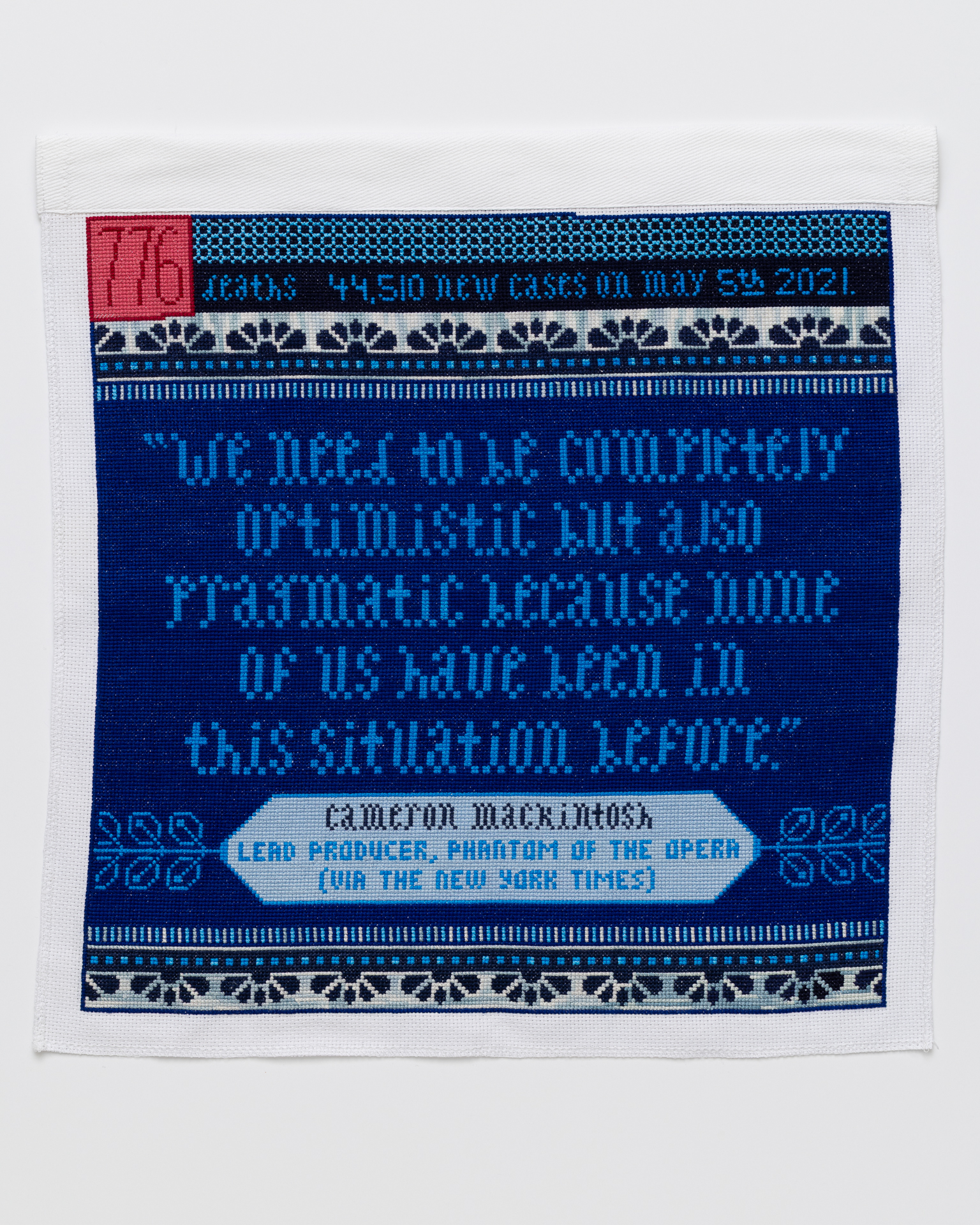 May 5, 2021 Cross stitch embroidery in blue threads with pink and red square in top left corner "776" written inside the square. The top strip of the piece reads "deaths 44, 510 new cases on may 5th 2021." below that is a pattern of scallops in dark blue, with a line of blue dots and stripes beneath it. In the middle is a quote: "we need to be completely optimistic but also pragmatic because none of us have been in this situation before." In the bottom is a light blue diamond shape with "Cameron Mackintosh Lead Producer, Phantom of the Opera (via the New York Times) written. The stripe/dot/scallop pattern is repeated at the bottom.
