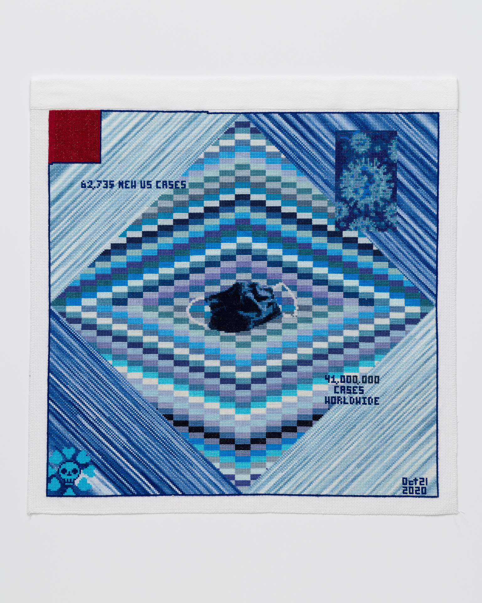 Cross stitch embroidery of random lines of blue in diamond shape. A dark blue face mask is in the middle. An image of the COVID virus is in the upper left. A skull and cross bones in the lower left cornee. "Oct 21, 2020" is in the lower right corner. There is a red square in the top left corner. "62,375 NEW US CASES" is in the upper left, "41,000,000 CASES WORLDWIDE" in the lower right.